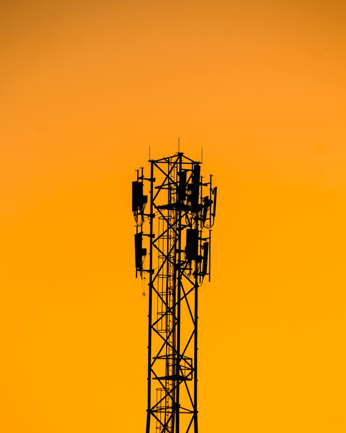 gallery-4 A telecommunication tower silhouetted against a vibrant orange sunset sky in India.