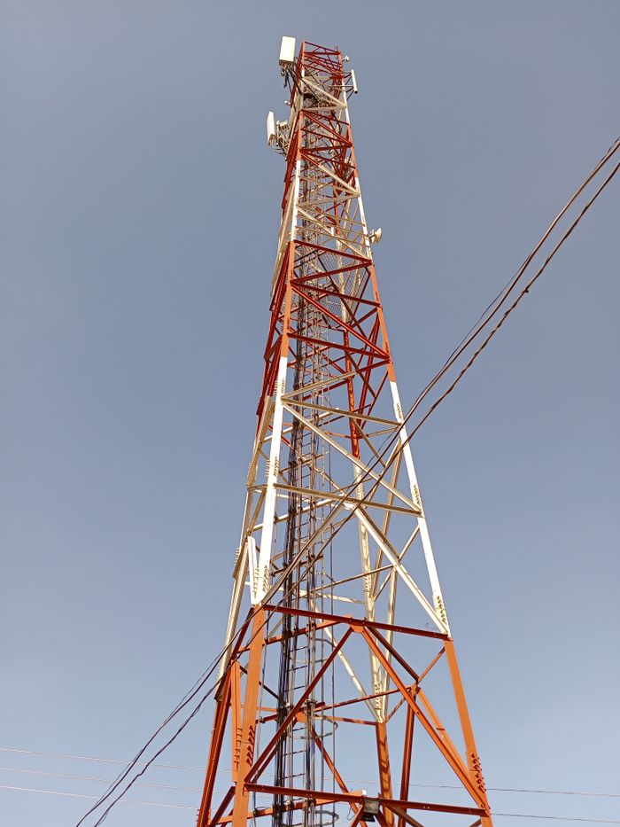 contact-img Low angle view of a tall red and white telecommunication tower against a clear blue sky.