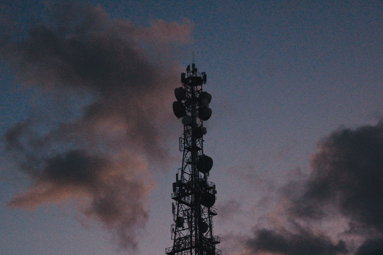 services-02 Silhouette of a telecommunications tower against a vibrant twilight sky with clouds.
