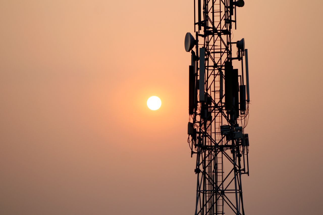 about-01 A striking silhouette of a communication tower against a vibrant sunset sky.